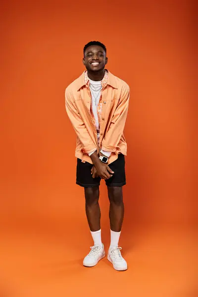 Stylish young man in orange shirt and shorts strikes a pose. — Stock Photo