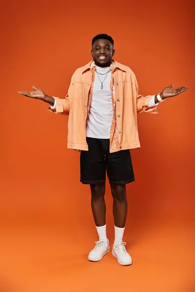 Handsome man in fashionable orange shirt and shorts standing confidently against vivid orange backdrop. — Stock Photo