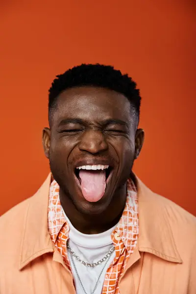 Handsome African American man playfully sticks out his tongue against a vibrant orange backdrop. — Stock Photo
