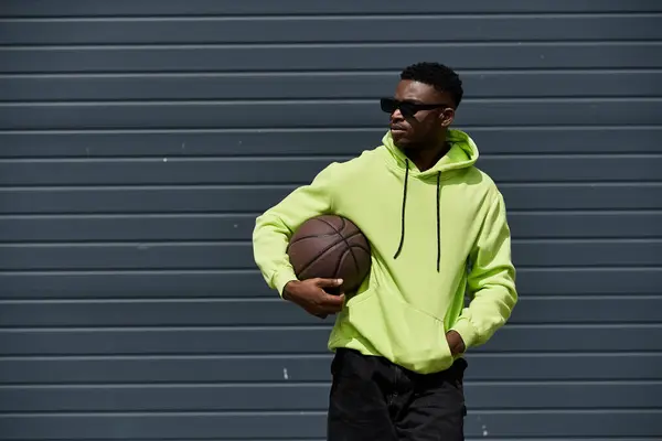 Afroamerikaner in grünem Kapuzenpullover hält Basketball. — Stockfoto