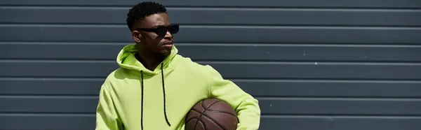 Schöner afroamerikanischer Mann in grünem Kapuzenpullover hält Basketball. — Stockfoto