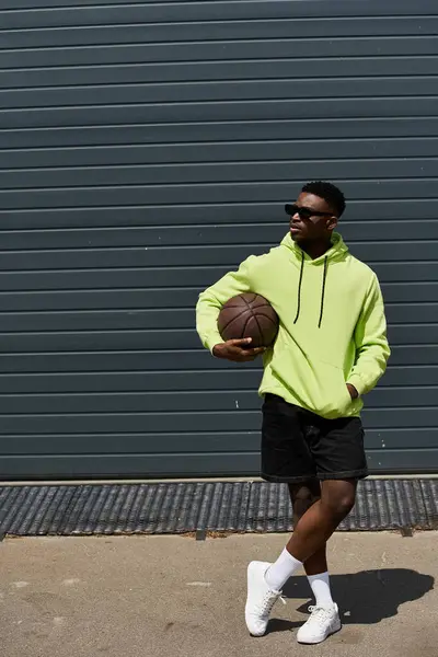 African American man in trendy neon green hoodie holds basketball. — Stock Photo
