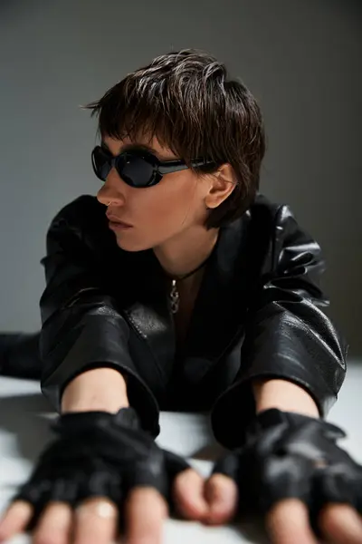 Stylish woman in black leather jacket and gloves posing on a table. — Stock Photo