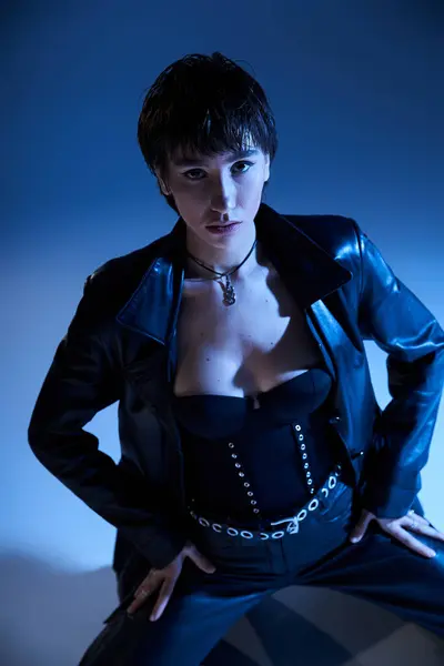 Stylish woman strikes a pose in black leather on blue. — Stockfoto