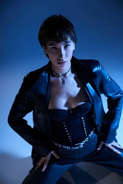 Stylish woman strikes a pose in black leather on blue. — Stock Photo