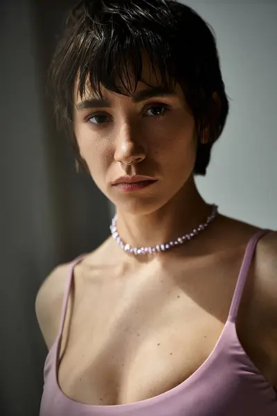 A beautiful young woman in a pink top and necklace strikes a stylish pose. — Photo de stock