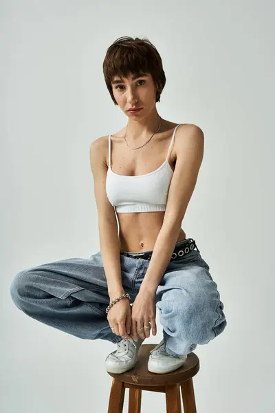 Young woman in white top, jeans, posing on stool. — Stockfoto