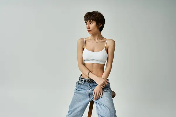Young woman in jeans and white top sits calmly on a stool. - foto de stock