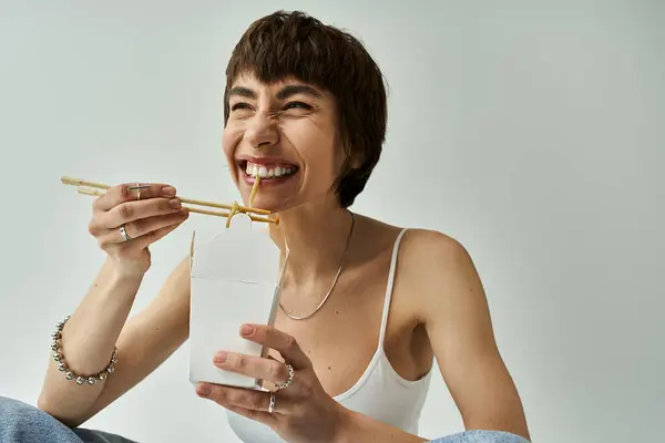 Young woman enjoying noodles with chopsticks on white background. — Stockfoto