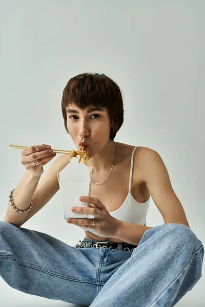 A stylish woman enjoying noodles while seated on the floor. — Stock Photo