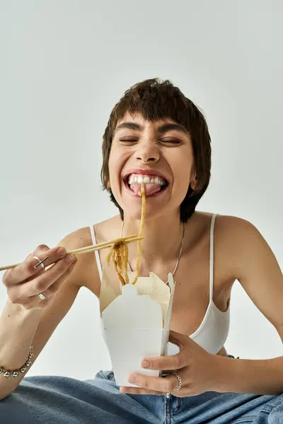 Stylish woman savoring noodles with chopsticks against a white backdrop. — Stockfoto