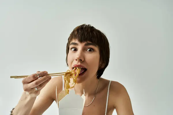 Stylish woman enjoys noodles with chopsticks. — Stock Photo