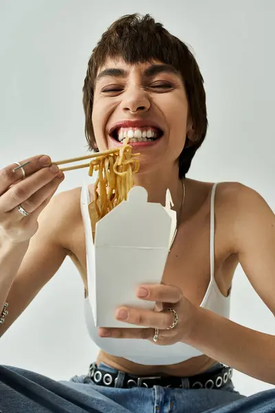 A stylish young woman gracefully enjoying noodles with chopsticks. — Stock Photo