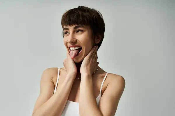 Young woman in stylish attire playfully sticking out tongue against white background. — Stock Photo
