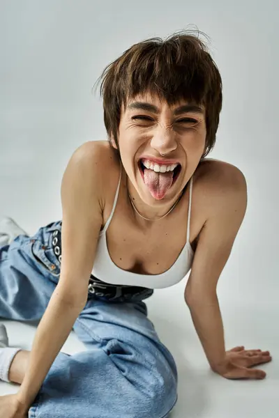 A stylish woman sticks out her tongue while laying on the floor. — Stockfoto