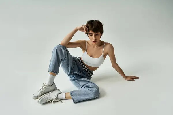 Stylish woman in white top and jeans sitting gracefully on floor. — стоковое фото