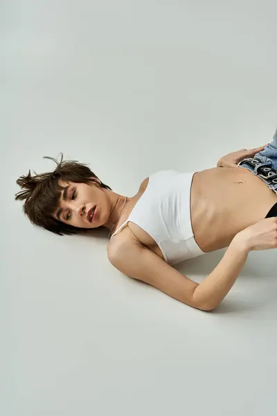 Young woman in white tank top and denim shorts lying on floor. — Photo de stock
