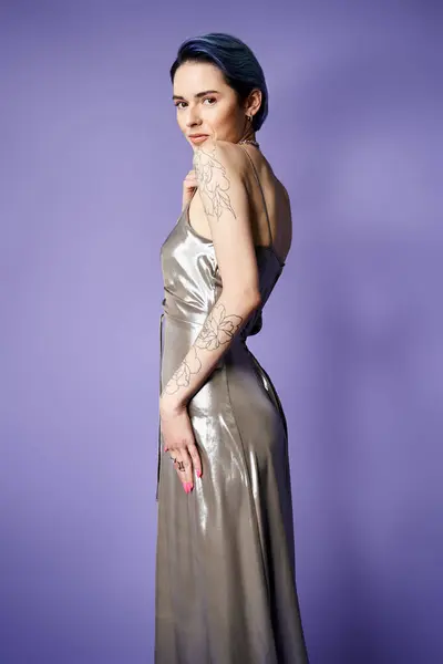 A young woman with short blue hair striking a glamorous pose in a shiny silver dress in a studio setting. — Foto stock