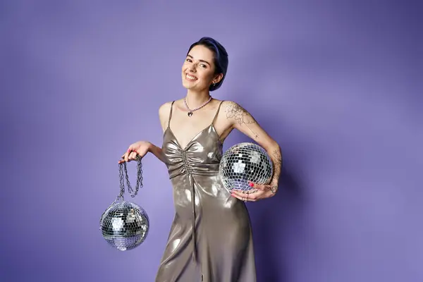A stylish woman in a silver dress holding two disco balls, radiating glamour and fun in a studio setting. — Stock Photo