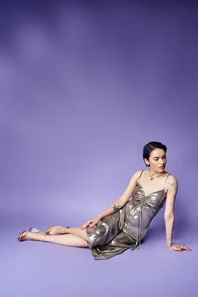 A young woman with short blue hair lays gracefully on the ground in a shimmering silver dress. — Fotografia de Stock