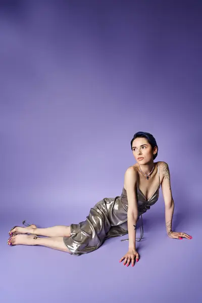 A young woman with short blue hair, wearing a silver dress, lies gracefully on the ground in a studio setting, exuding elegance. — Fotografia de Stock