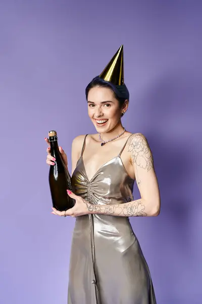 Young woman with short blue hair poses in silver party dress, holding a bottle, wearing a festive party hat. — Fotografia de Stock