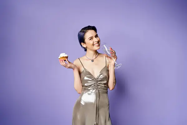 A stylish young woman with short blue hair is elegantly holding a delicious cupcake in a silver party dress. — Stockfoto