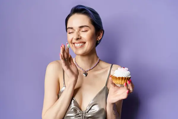 Young woman with short blue hair in a silver party dress holding a vibrant cupcake, exuding elegance and charm. — Stock Photo