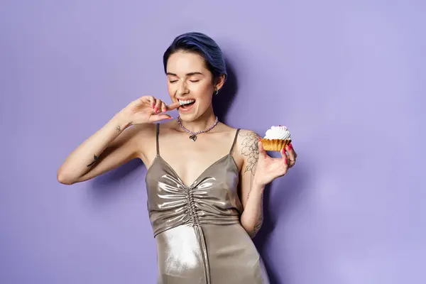 A young woman with short blue hair elegantly holds a cupcake, showcasing a silver party dress in a studio setting. — Fotografia de Stock