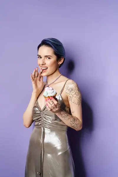 Young woman with short blue hair wearing silver dress elegantly holds a cupcake in a studio setting. — Fotografia de Stock