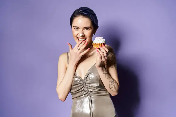 A young woman with short blue hair strikes a pose in a silver party dress while delicately holding a cupcake. — Stockfoto