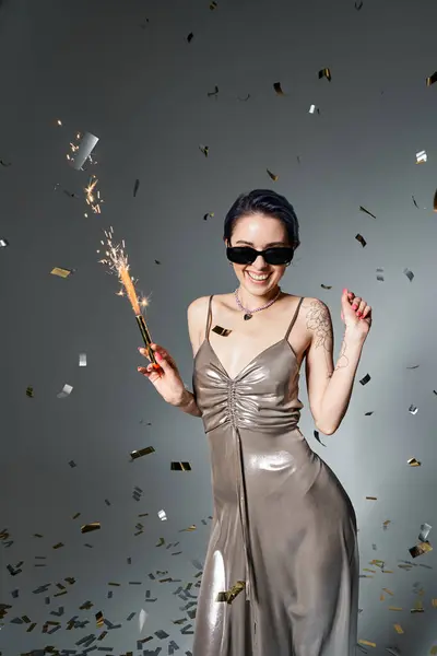 A young woman with short blue hair strikes a pose in a silver party dress, holding a sparkler with a sparkle in her eyes. — Stock Photo