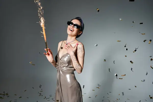 A young woman with short blue hair dazzles in a silver dress while holding a sparkler in a studio setting. — Stock Photo