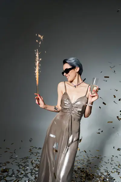Young woman in silver dress and blue hair holding sparkler, radiating elegance and charm in a studio setting. — Stock Photo