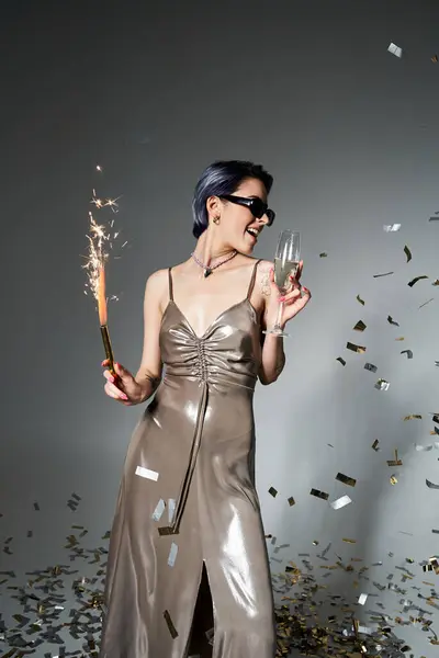 A stylish young woman with short blue hair looks elegant in a silver dress while holding a glass of champagne. — Fotografia de Stock