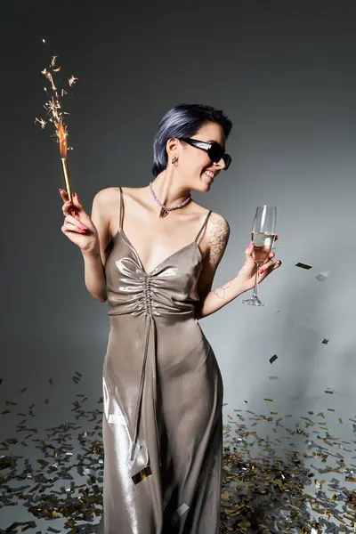 Young woman with short blue hair in silver party dress gracefully holds a glass of champagne. — Stock Photo