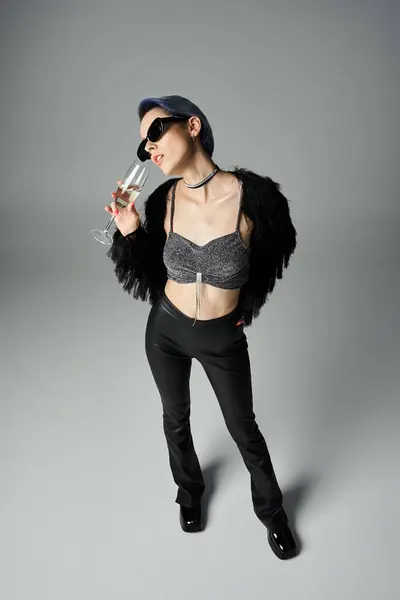 A chic young woman in a bra top and black pants, holding a champagne glass in a stylish studio setting. — стоковое фото