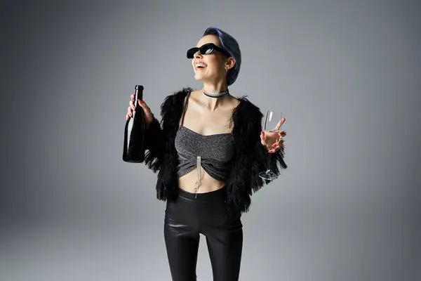 A stylish young woman with short dyed hair, wearing a black top and leggings, holds a champagne bottle — стокове фото