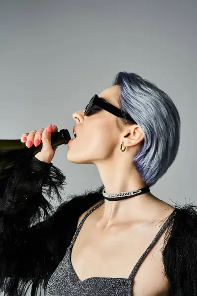 Stylish young woman with blue hair and sunglasses sipping from a bottle. — Stockfoto