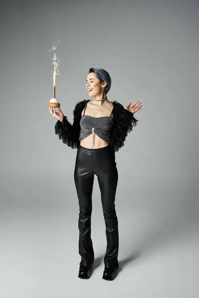 Young woman with short dyed hair in black leather pants holding a cupcake. — стоковое фото