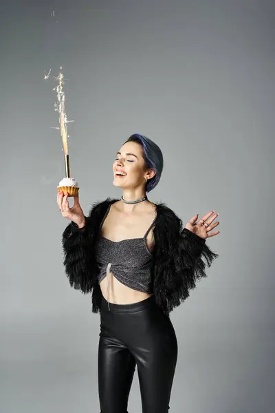 A young woman with short dyed hair wearing black pants and a crop top, playfully holds a sparkler in a studio setting. — стоковое фото