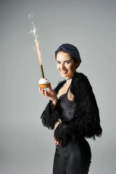 A young woman with short, dyed hair posing in stylish attire, holding a cupcake with a sparkler. — стоковое фото
