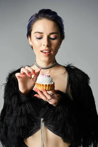 Stylish young woman in chic black outfit holding a delicious cupcake. — Fotografia de Stock