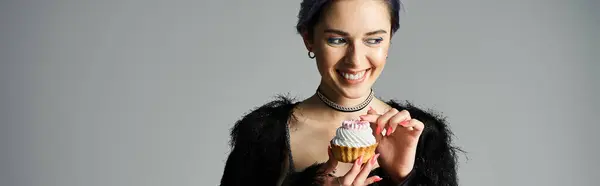 Stylish birthday girl with dyed hair holds a scrumptious cupcake in her hands. — стокове фото