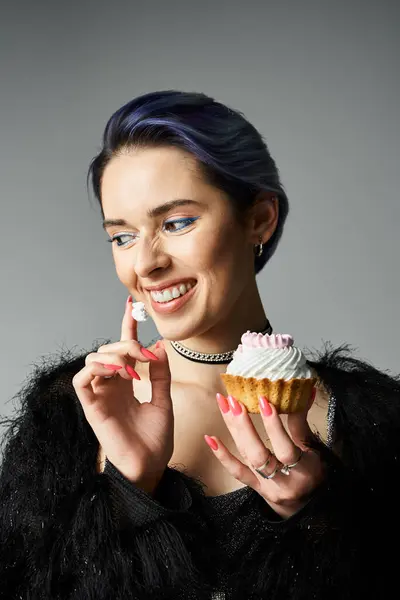 A stylish young woman with blue hair holding a delicious cupcake in a photo studio setting. — стокове фото