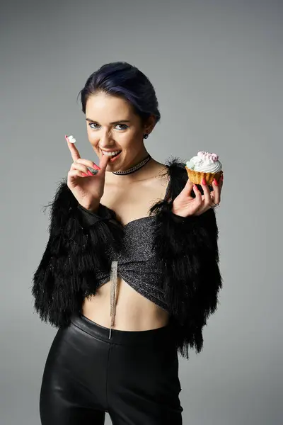 Young woman in black jacket holds a cupcake elegantly. — Fotografia de Stock
