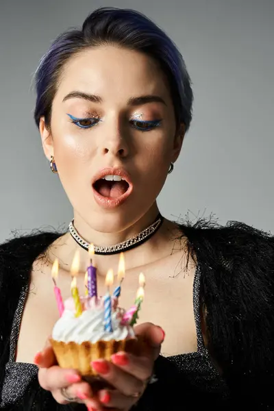 Stylish young woman holds a cupcake topped with lit candles. — Stock Photo