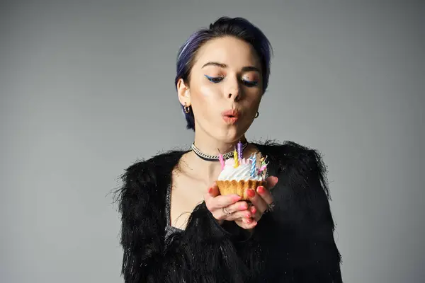 A stylish young woman with short dyed hair, blowing out candles on a cupcake in celebration. — Foto stock
