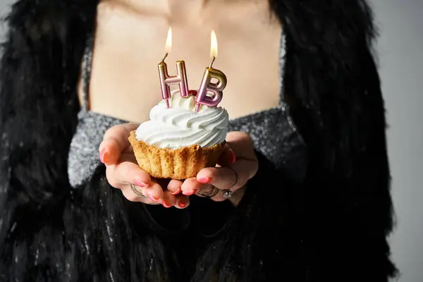 A stylish young woman with short dyed hair holding a cupcake with burning candles in a studio setting. — стокове фото