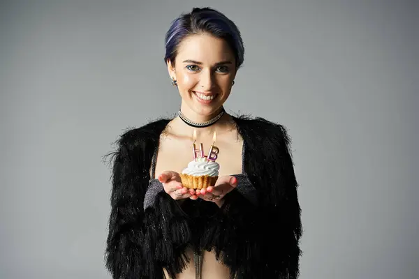 Young woman with short dyed hair holding a cupcake with icing, in stylish attire, in a studio setting. — Photo de stock